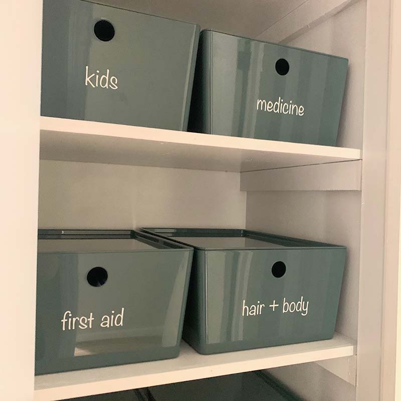 green storage bins with white text vinyl labels for "kids", "medicine", "first aid", and "hair + body"