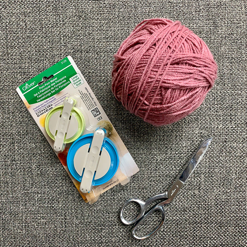 yarn, two Pom Pom makers, and a pair of scissors on carpet