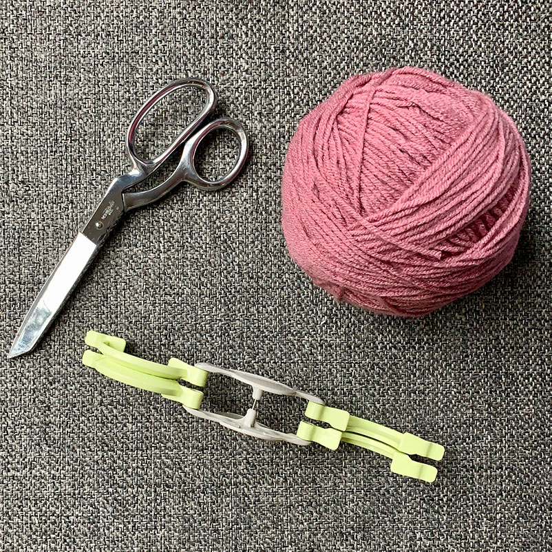 scissors, ball of pink yarn, and opened Pom Pom maker on carpet
