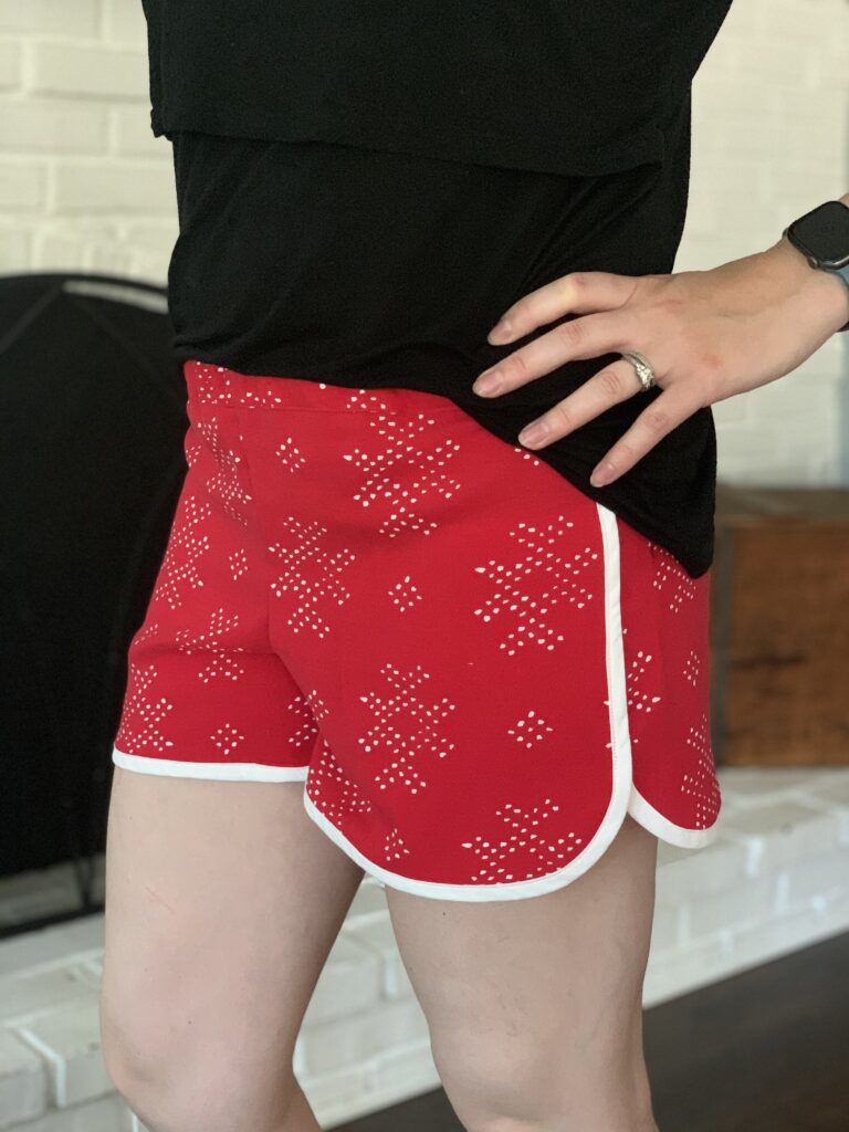 wearing a pair of City Gym Shorts by Purl Soho in geometric patterned red with white contrast bias tape