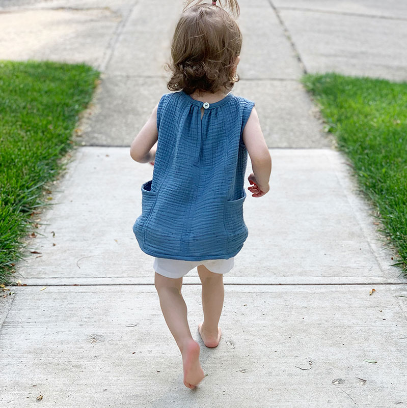 toddler girl wearing tank top with pockets full running down the sidewalk barefoot