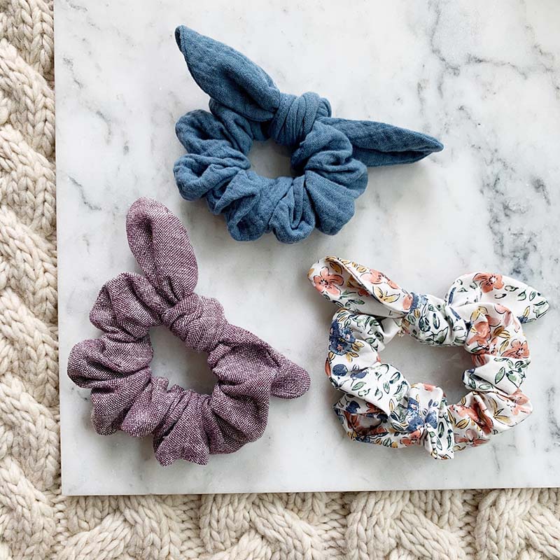 Learn how to sew a bow scrunchie. Three scrunchies placed on piece of marble over cabled blanket