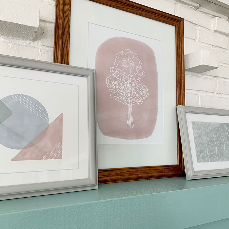 three framed art prints sit on a mantel