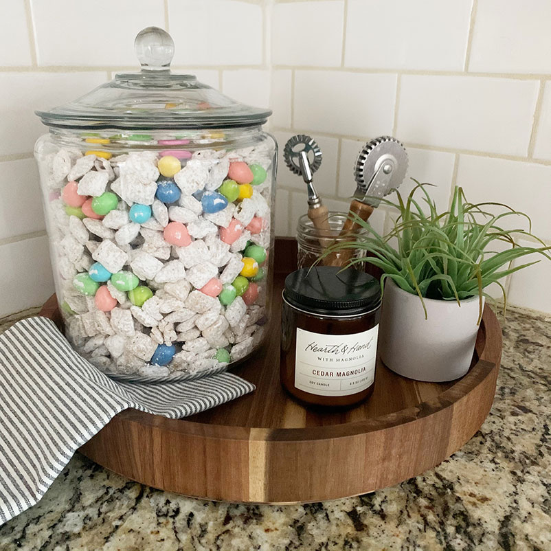 puppy chow with chocolate easter egg candies on display on the corner of a kitchen with candle, small plant, and kitchen utensils.