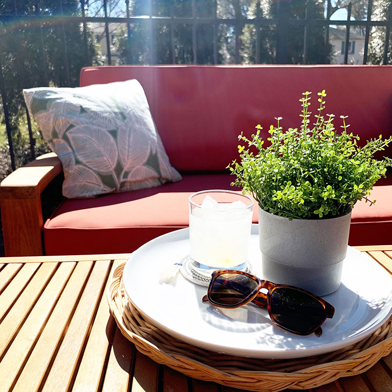 outdoor patio seating with coffee table in foreground with large plate holding plant, sunglasses, and a drink