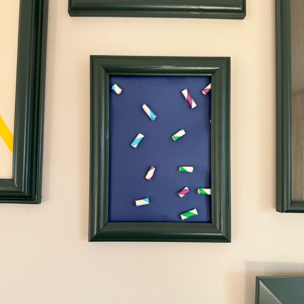 close up of a frame with a navy blue paper with blue, white, and purple striped straws glued to it