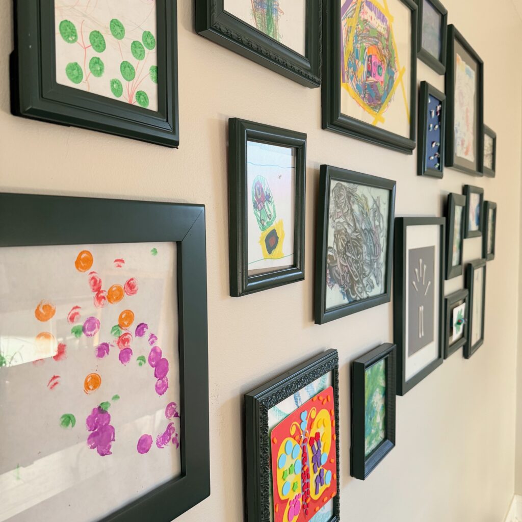 side view of gallery wall of kids art, featuring thrifted picture frames that were spray painted hunt club green 