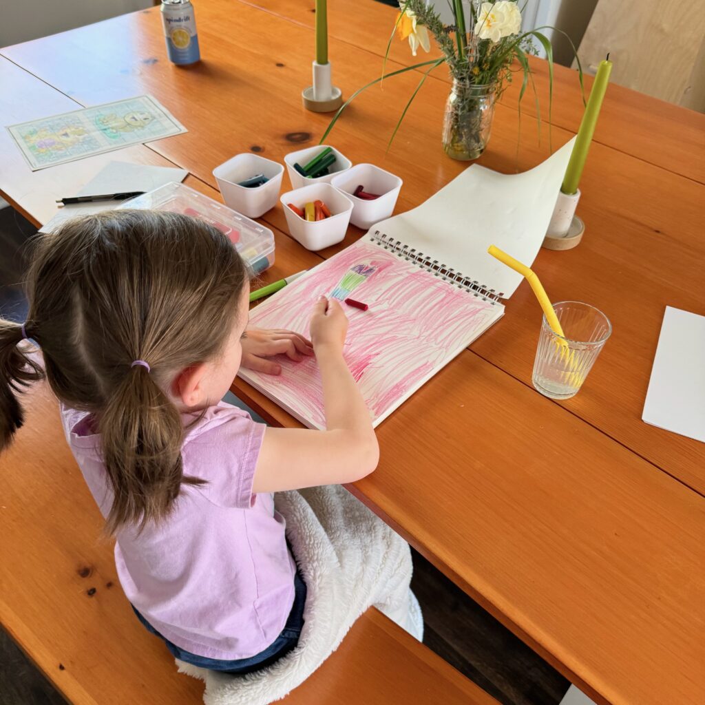 child coloring in a sketchbook on a dining room table