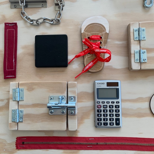 close up of closed mirror compact, velcro, shoe laces, hinged door, calculator, and zipper on DIY busy board.