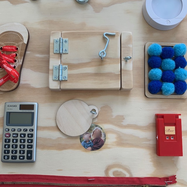 Close up of the calculator, stitch counter, pom poms, shoe laces, closed door, and a small piece of wood pushed to the side to reveal a photo of kids with their faces blurred out.