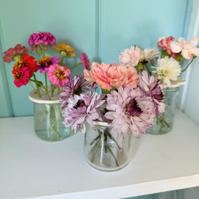 three small jars with an air dry clay flower frog on top holding a variety of flowers in place