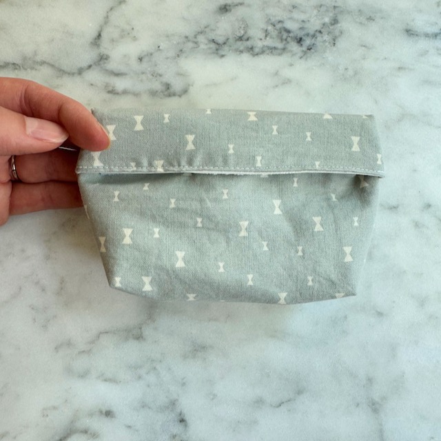 learn how to sew a reusable snack bag, someone holding a small blue fabric reusable snack bag on top of marble countertop